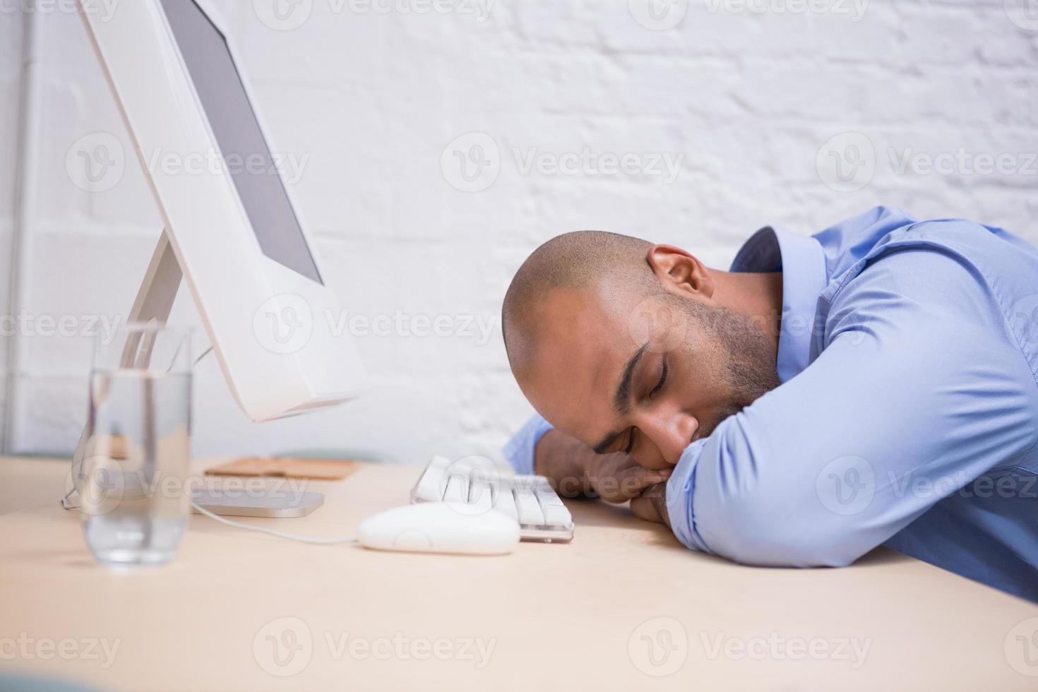 Geschäftsmann, der durch Computer am Schreibtisch schläft foto
