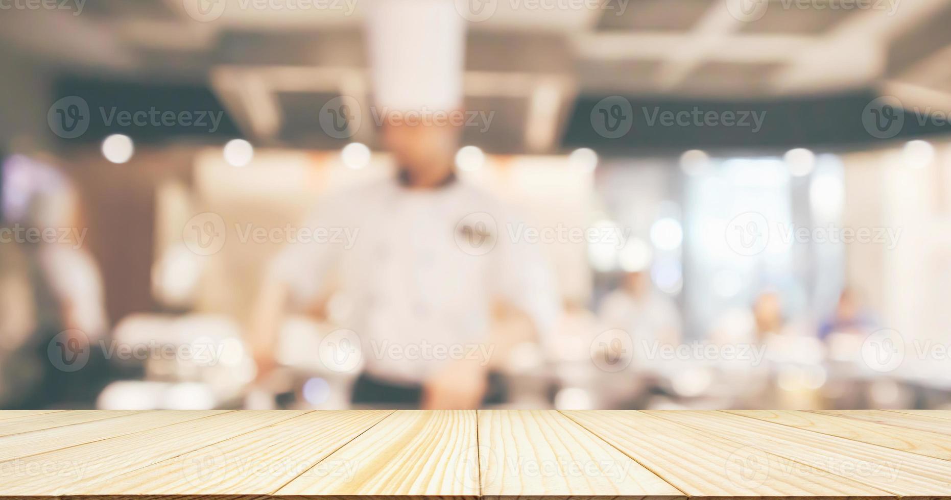 leere Holztischplatte mit Küchenchef, der in der Restaurantküche kocht, unscharfer, defokussierter Hintergrund foto