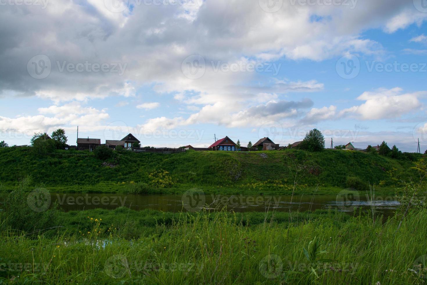 ein Dorf am Flussufer mit hellgrünem Gras und einem wunderschönen Himmel. foto