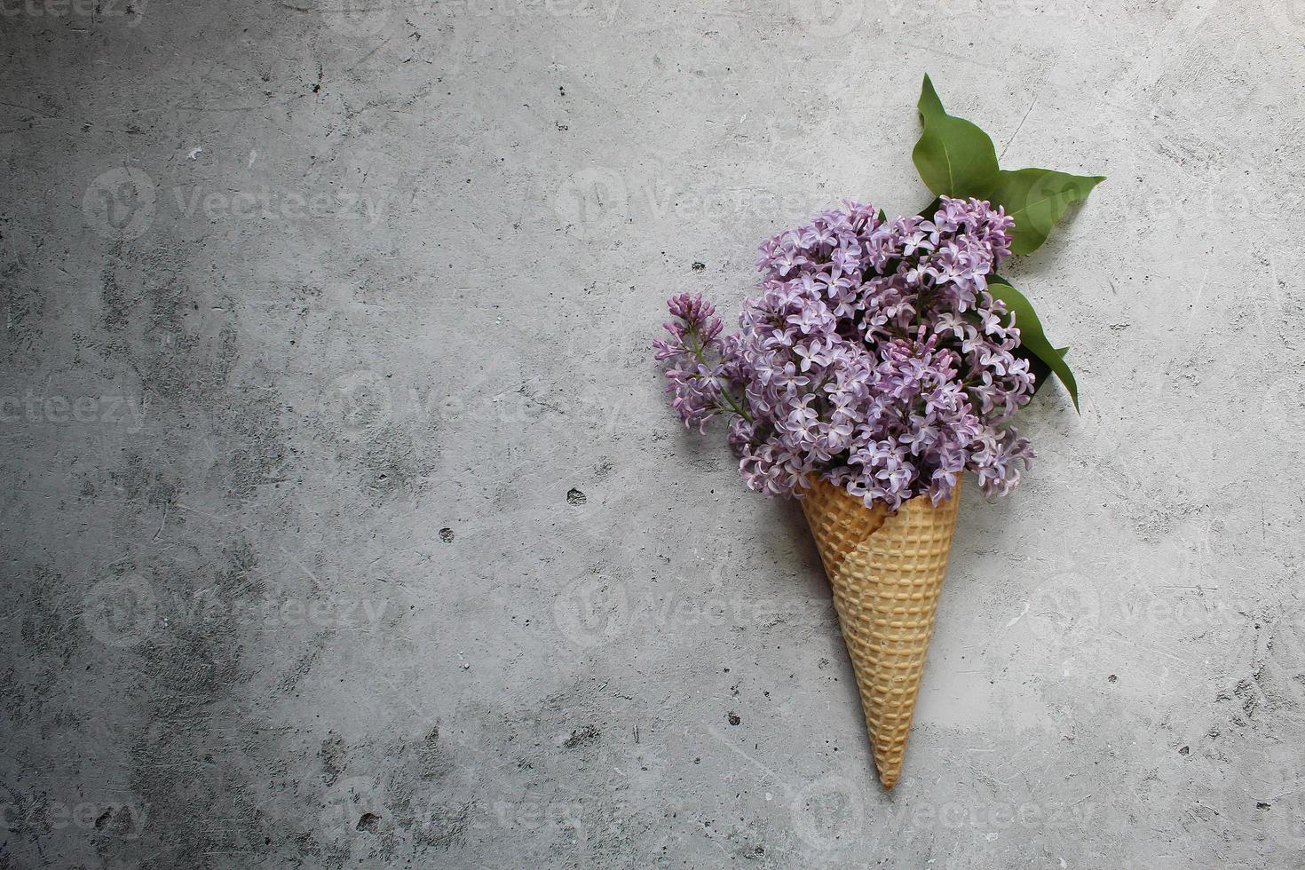 Eistüte mit bunten Blumen auf grauem Hintergrund. flach liegen. Minimales Sommerkonzept. foto