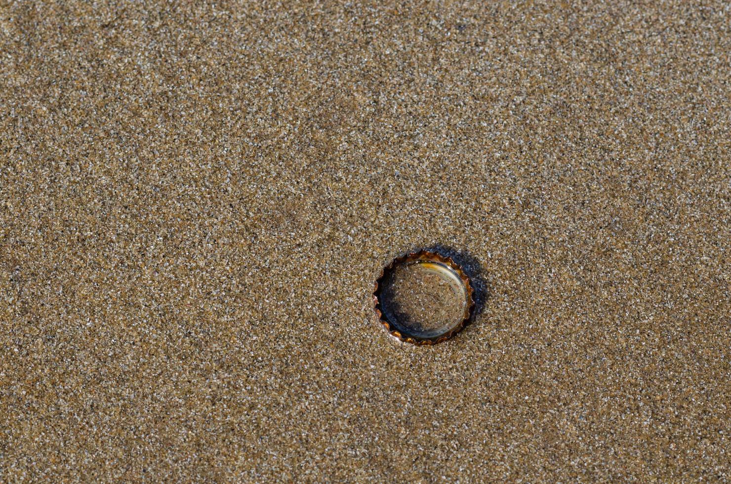 Eine alkoholfreie Getränkekappe mit Rost auf dem nassen, sauberen Sand des Strandes mit Schatten vom Sonnenlicht. foto