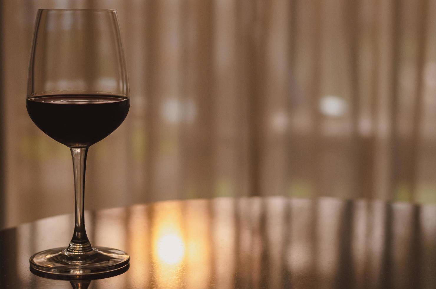 ein glas rotwein auf dem tisch im zimmer mit sonnenuntergangslicht auf curtian hintergrund. foto