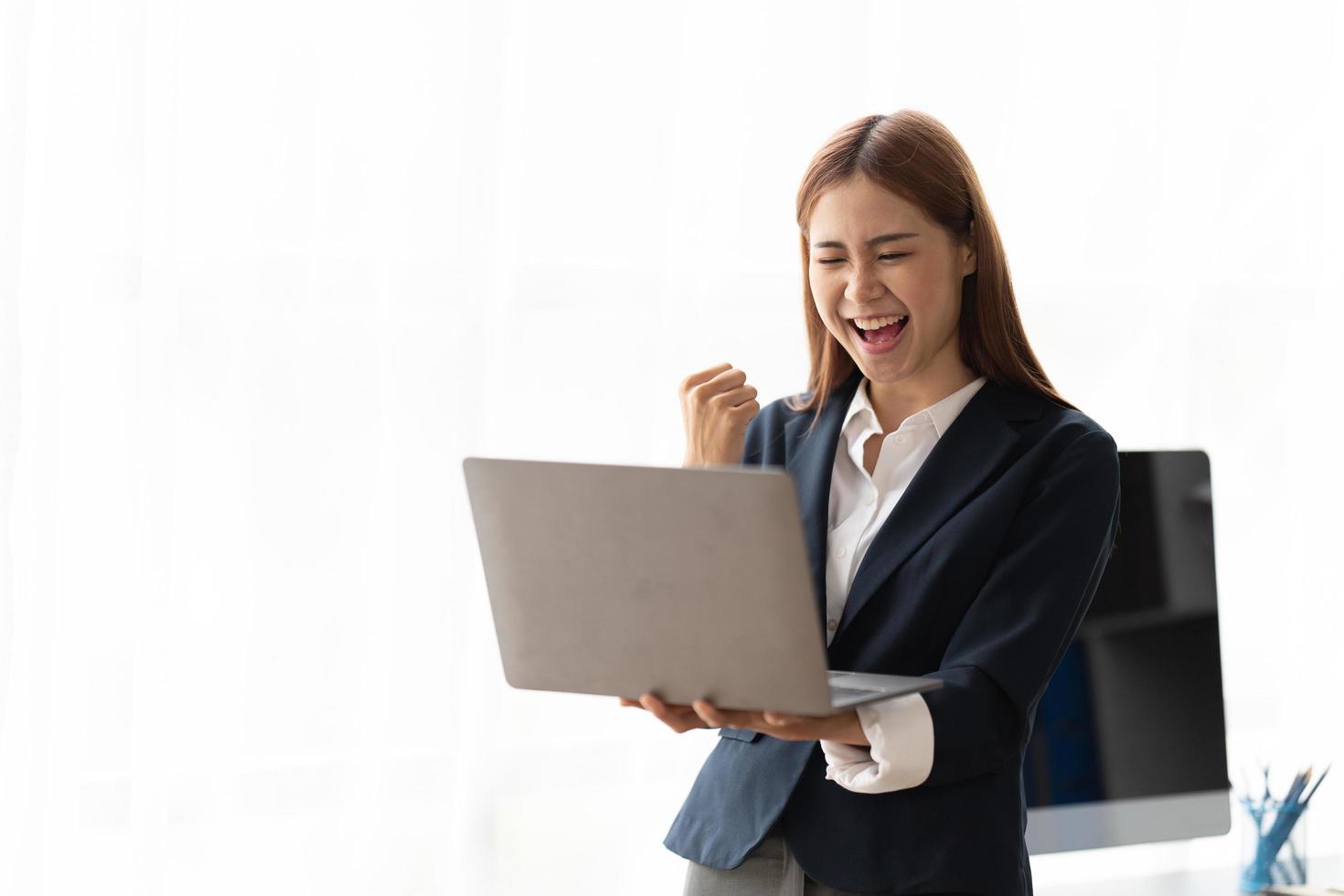 Porträt einer aufgeregten jungen asiatischen Geschäftsfrau, die Laptop-Computer hält und den Erfolg feiert, der über weißem Hintergrund, Kopienraum lokalisiert wird. foto