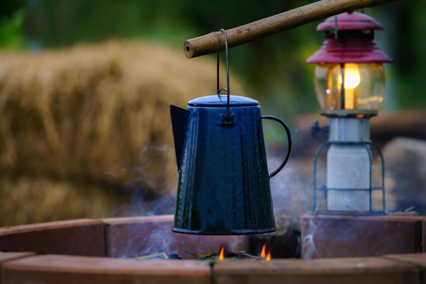 Emaille-Kaffeetasse, Vintage-Wasserkocher in Brand beim Nachtcamping. der hintergrund ist eine alte gaslaterne. weicher Fokus. flacher Fokuseffekt. foto