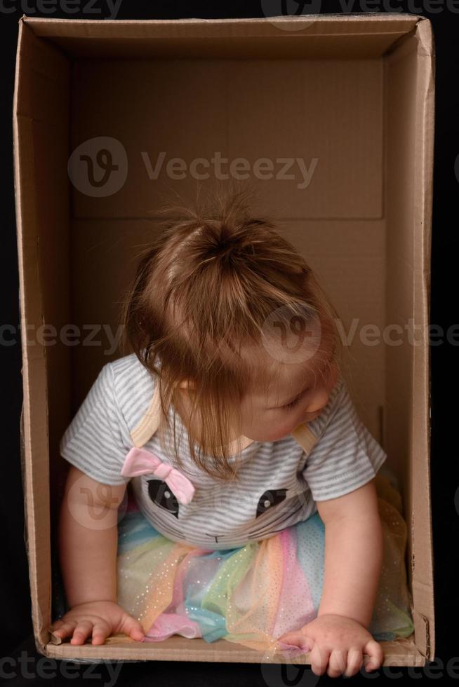 glückliches kleines Mädchen, das in einem Karton sitzt und Spaß hat foto