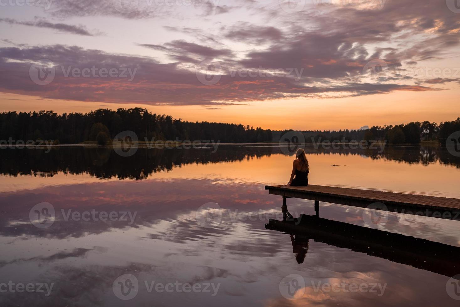 Einsame Mädchensilhouette bei Sonnenuntergang am See. foto