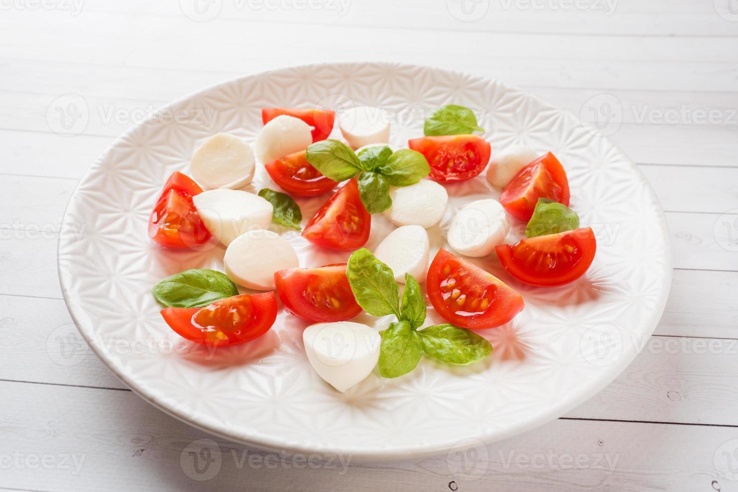 Caprese-Salat aus Tomaten, Mozzarella-Käse und Basilikum auf einem weißen Teller. italienische Küche. foto