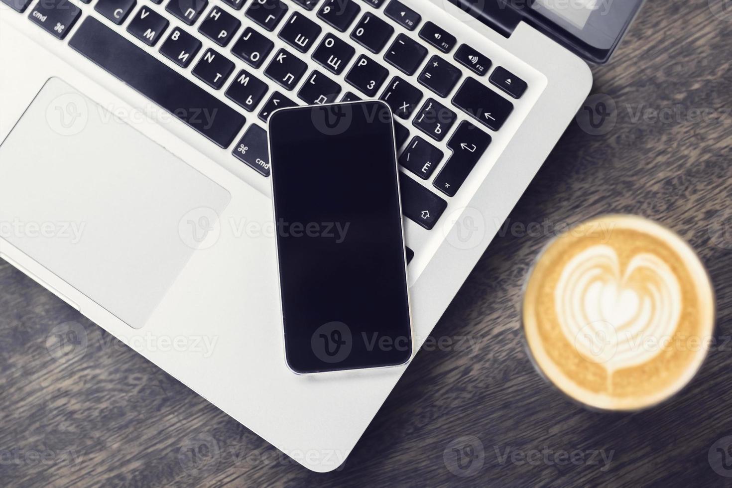 Laptop, Smartphone und Cappuccino auf einem Holztisch foto