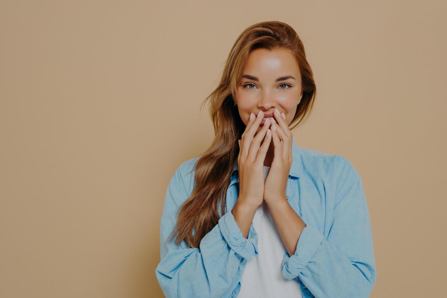 Fröhliches weibliches Modell mit fröhlichem Ausdruck bedeckt ihre Lippen mit den Händen foto