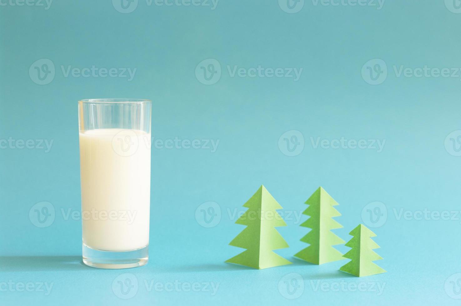 Glas Milch und grüner Origami-Wald auf blauem Hintergrund. foto