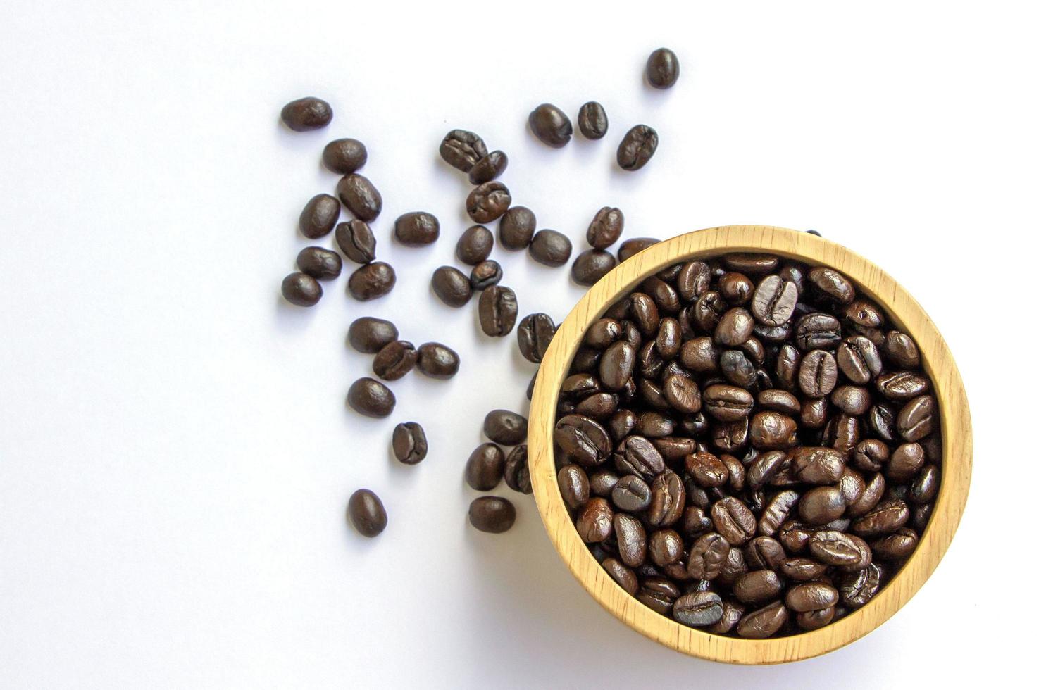 Bio-Arabica geröstete braune Kaffeebohnen in einer Holzschale auf weißem Hintergrund. konzept des frischen aromakoffeins foto