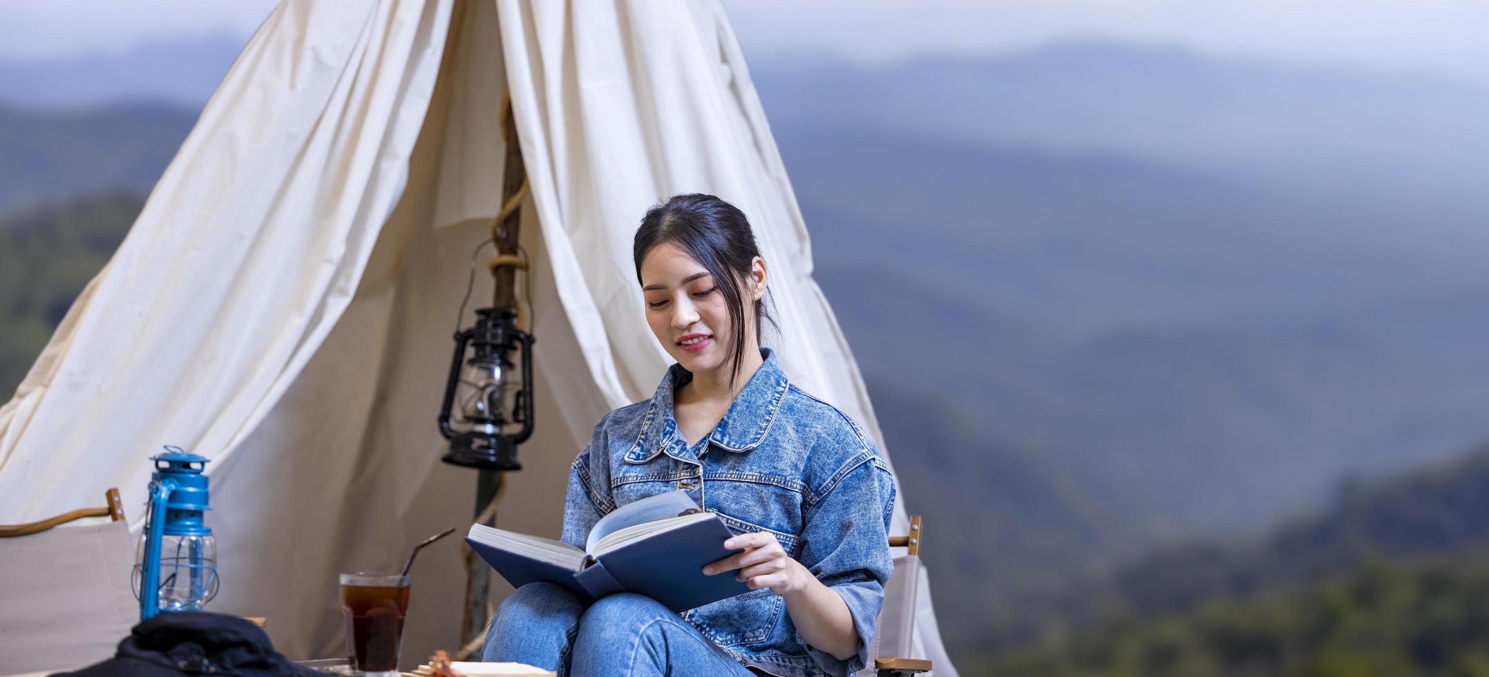 asiatische Frau liest Buch während eines Solo-Trekking-Camps auf dem Gipfel des Berges mit kleinem Zelt für Wochenendaktivitäten und Outdoor-Verfolgungskonzept foto