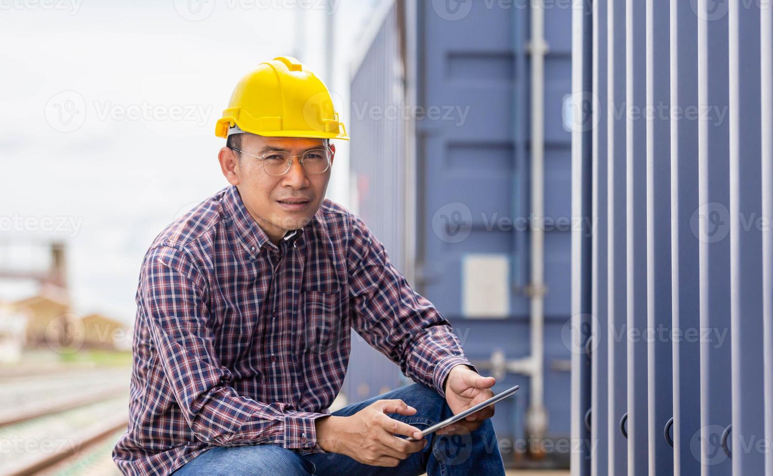 entspannender ingenieurmann in industriecontainern fracht, vorarbeiter dockarbeiter in helm und sicherheitsweste kontrollieren das laden von containern aus der fracht foto