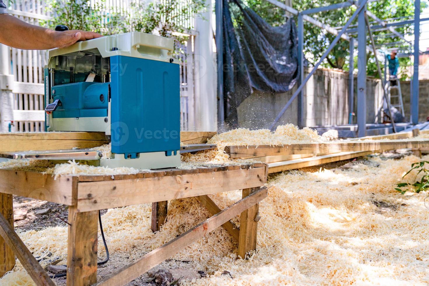 Arbeiter schrubbt die große lange Holzplatte mit Poliermaschine im Garten. foto