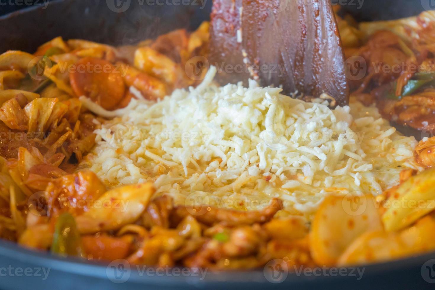 tokboki koreanisches traditionelles essen heißer und würziger reiskuchen, kombination und puff mit käse und gemüse auf dem schwarzen tisch auftragen foto