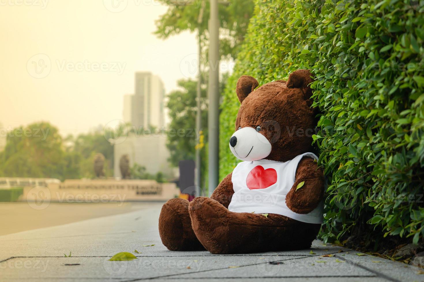 Dunkelbraune Bärenpuppe, die in einsamer Stimmung auf dem Fußweg neben der Straße sitzt. foto