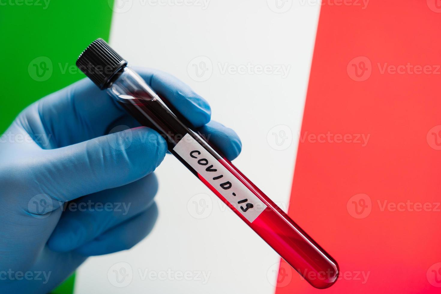 Epidemie-Alarm. Ausbruch des Coronavirus in Italien. testen sie die blutprobe in der hand mit medizinischen handschuhen gegen die italienische flagge. Gesundheitspersonal hält Reagenzglas foto