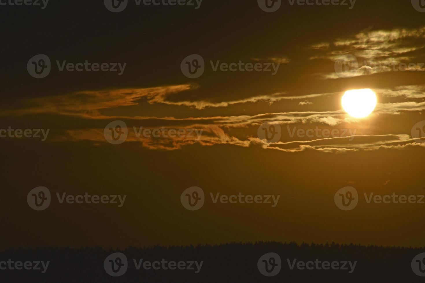 die Sonnenscheibe und Abendwolken im Hintergrund des Waldes foto