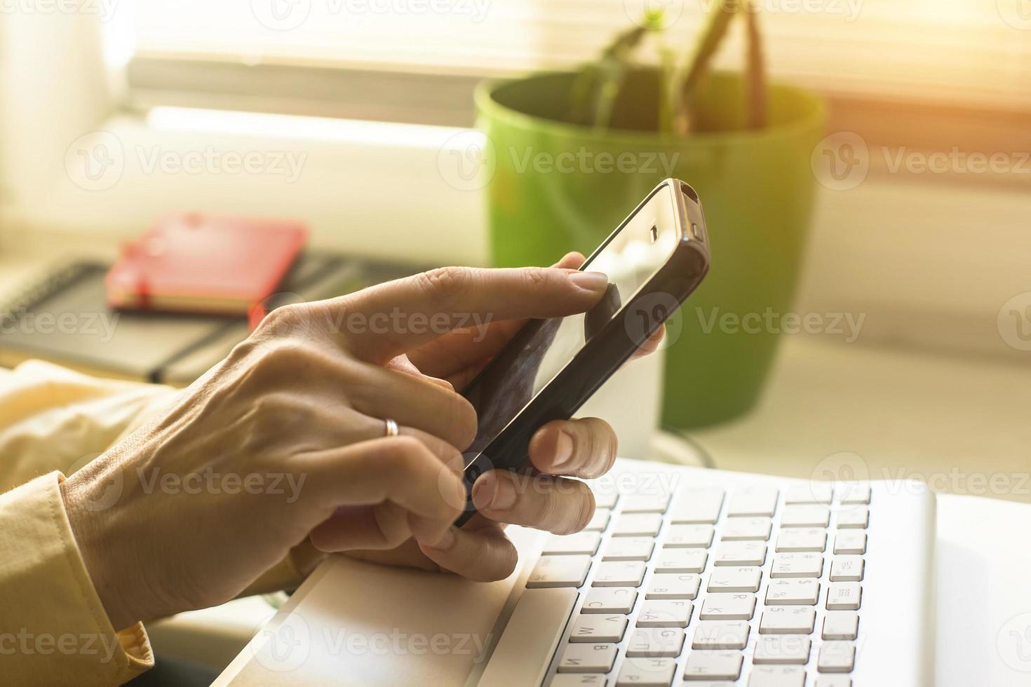 Frau mit Handy, Computertastatur im Hintergrund. foto