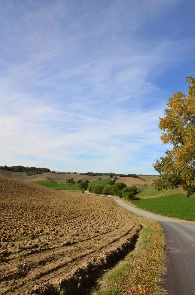 Gepflügtes Feld und kurvenreiche Straße in der Toskana foto