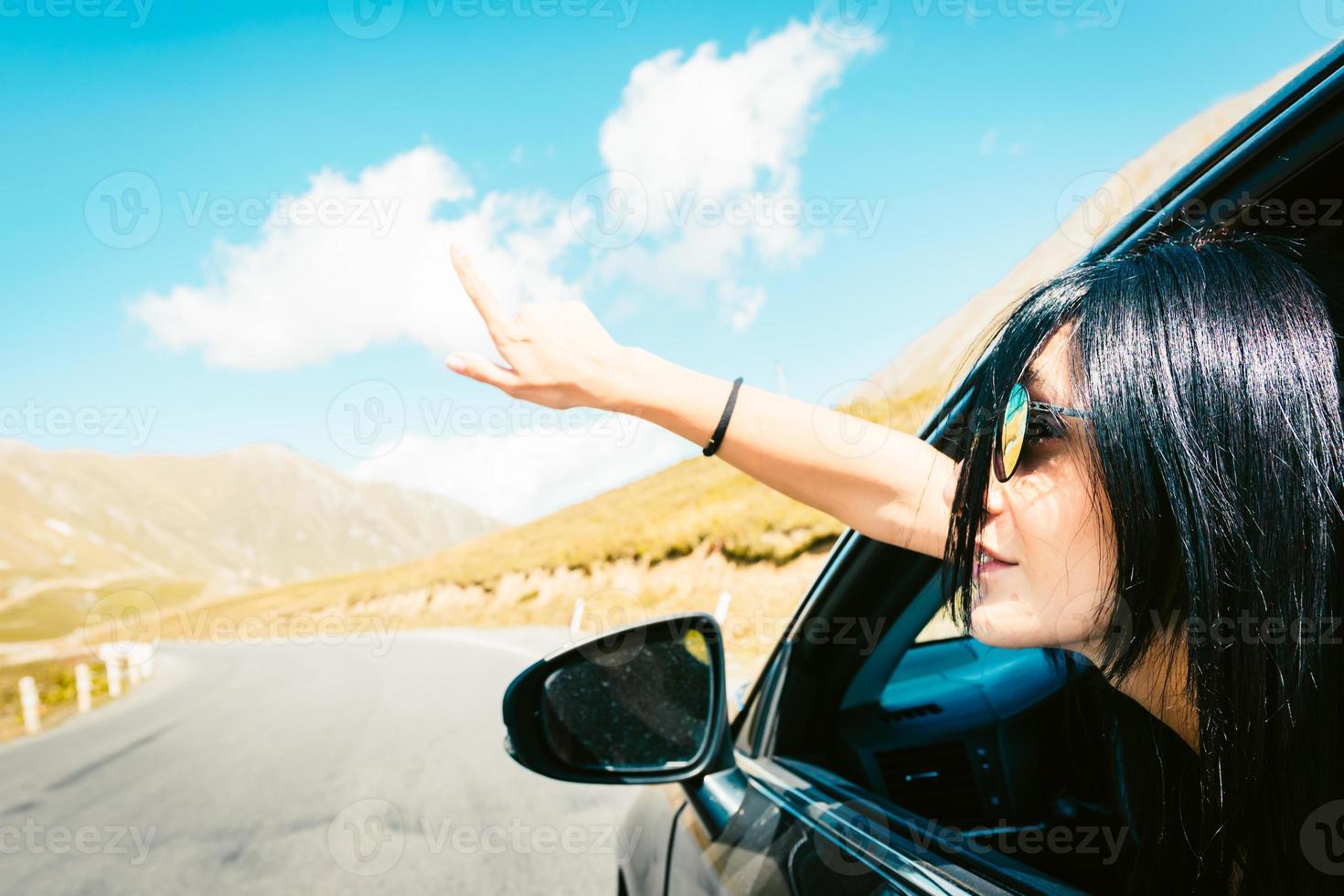 weibliche kaukasische frau vom autofenster zeigt finger nach links mit asphaltstraßenhintergrund. Roadtrip-Konzept kopieren. foto