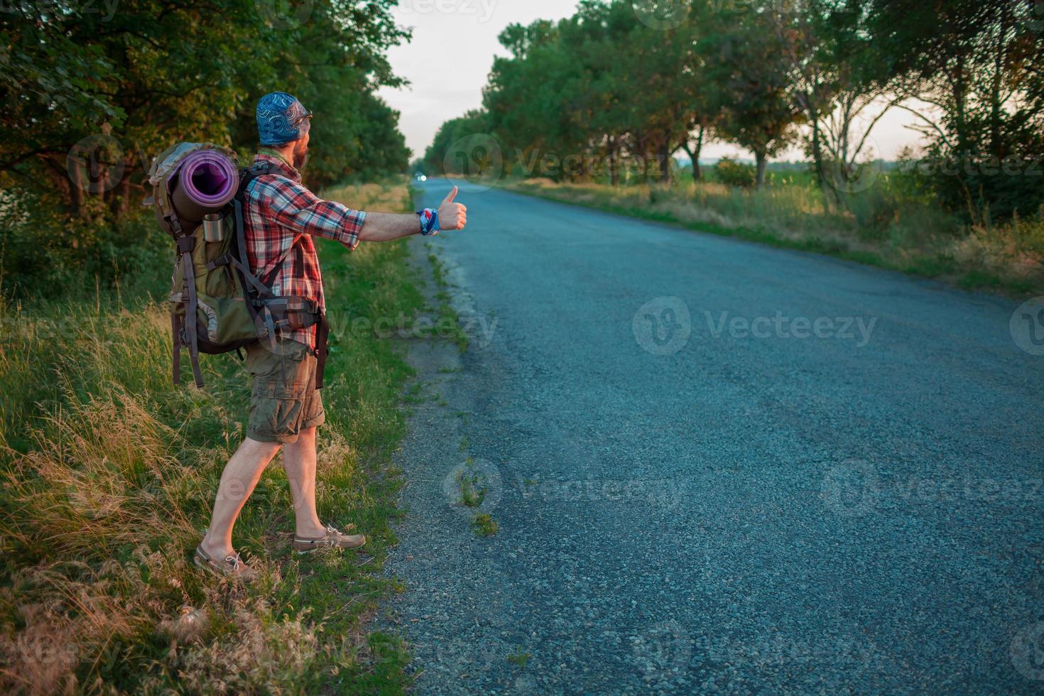 junger kaukasischer Tourist, der entlang einer Straße per Anhalter fährt foto