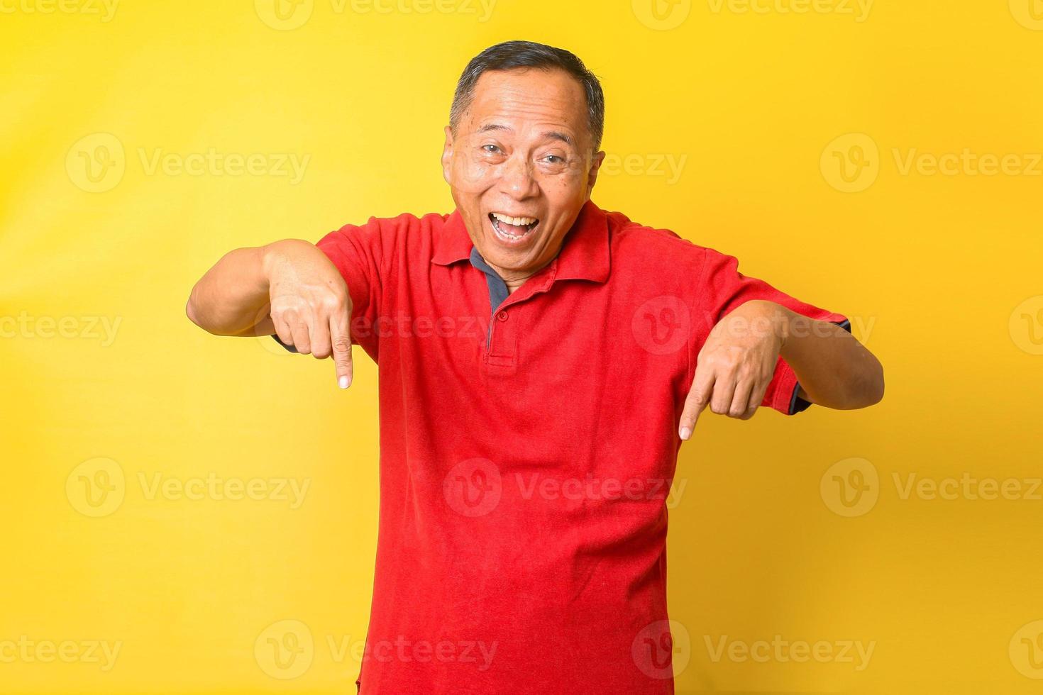 Attraktiver asiatischer älterer Mann im roten T-Shirt, der lächelt und mit dem Finger nach unten zeigt und versucht, auf wichtige Informationen zu achten. foto