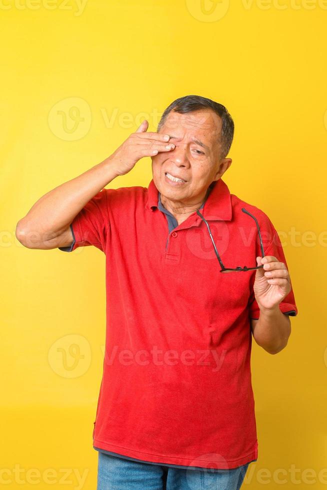 Der asiatische Senior fühlt sich müde, nachdem er mit einer Brille auf gelbem Hintergrund gelesen hat. alter mann mit augenreizung, optisches problem. foto