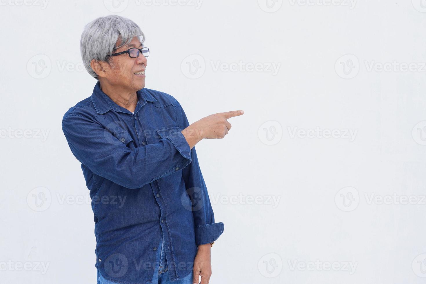 Asiatischer Senior im Denim-Casual-Stil zeigt mit dem Zeigefinger isoliert auf weißem Hintergrund mit Kopierraum. foto