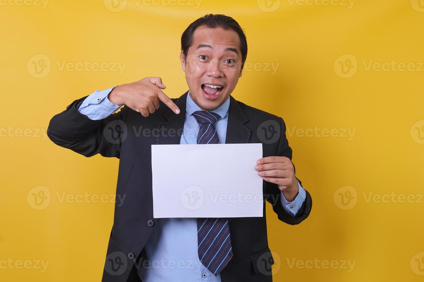 attraktives asiatisches junges erfolgreiches angestelltes unternehmen im anzug arbeiten im büro zeigen mit dem finger auf papierkontodokumenten isoliert auf gelbem hintergrund. foto