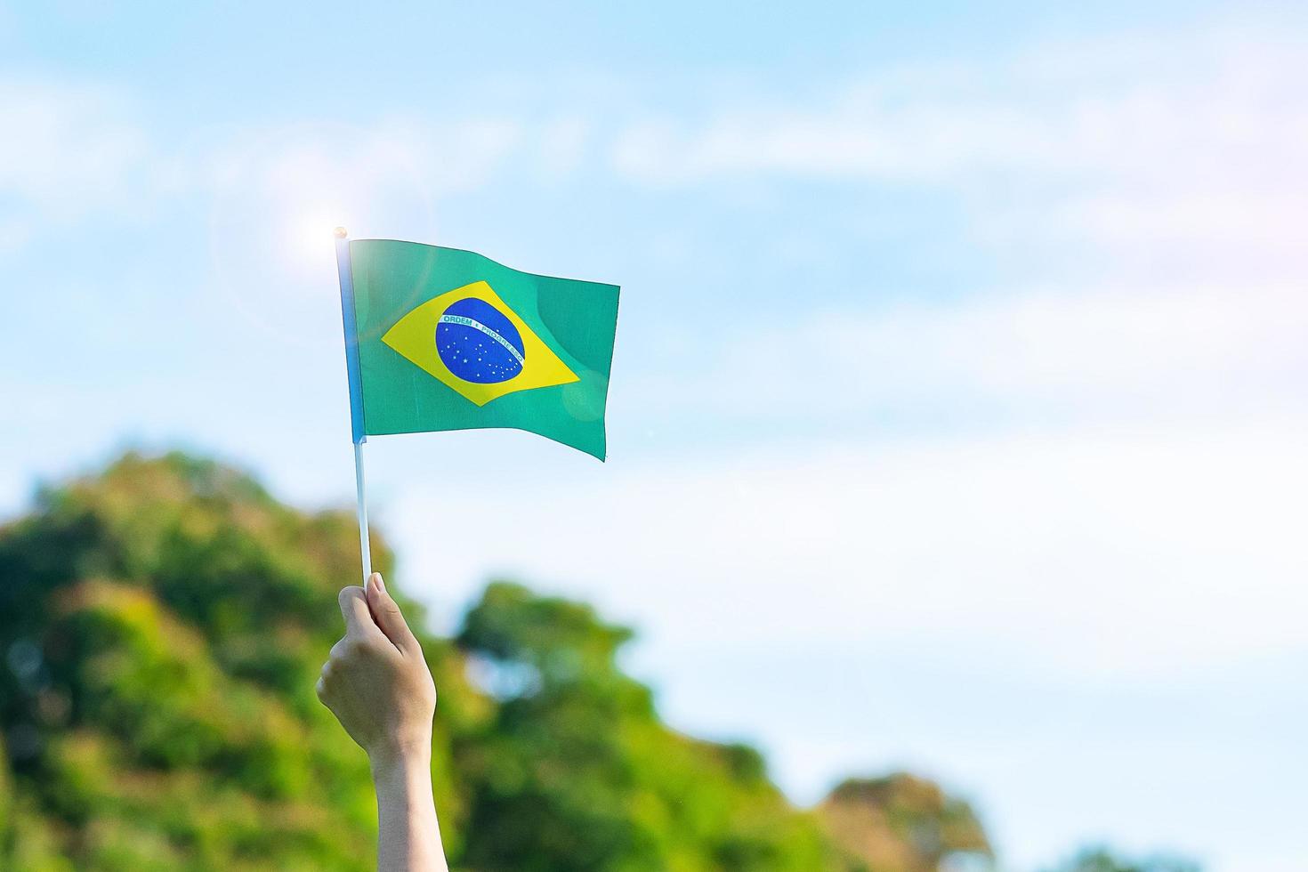 Hand, die Brasilien-Flagge auf Hintergrund des blauen Himmels hält. september unabhängigkeitstag und fröhliche feierkonzepte foto
