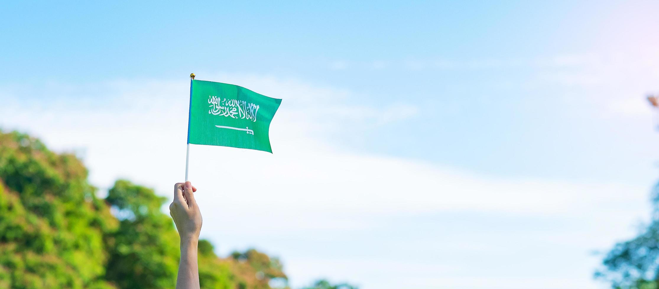 Hand, die Saudi-Arabien-Flagge auf Hintergrund des blauen Himmels hält. september saudi-arabien nationalfeiertag und fröhliche feierkonzepte foto