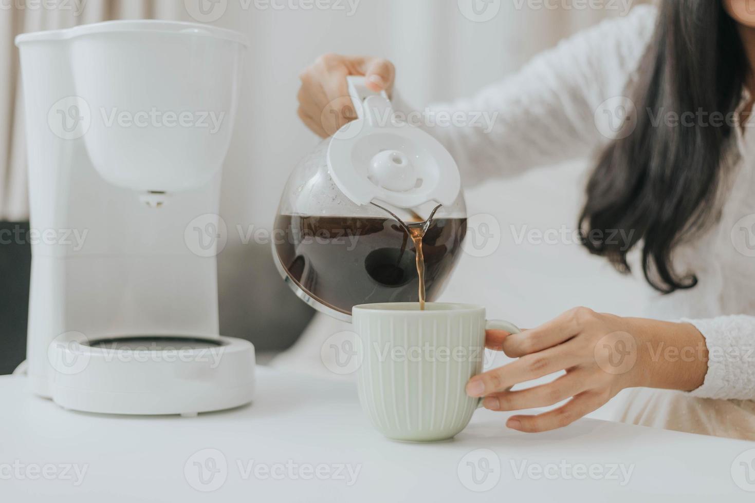 junge glückliche Frau mit Kaffeemaschine zu Hause. asiatische frau, die kaffee in eine tasse gießt und zu hause kaffee kocht. foto