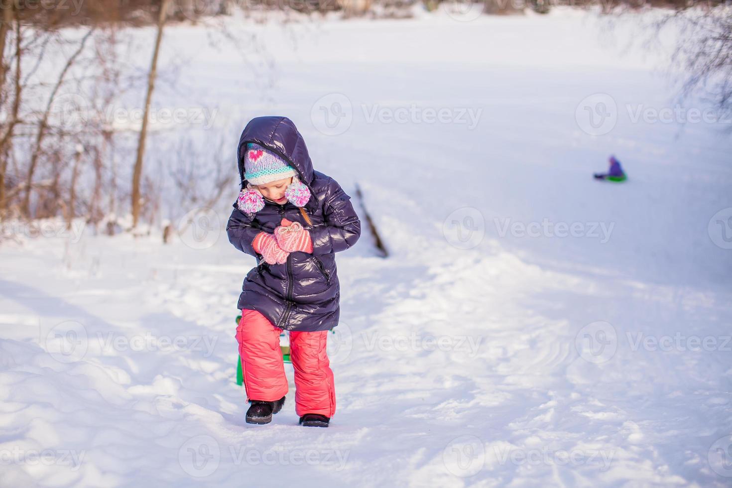 kleines entzückendes glückliches Mädchen, das schneesonnenen Wintertag genießt foto