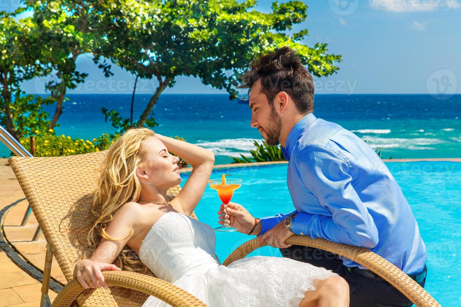 glückliche Braut und Bräutigam genießen einen Cocktail am Pool unendlich foto