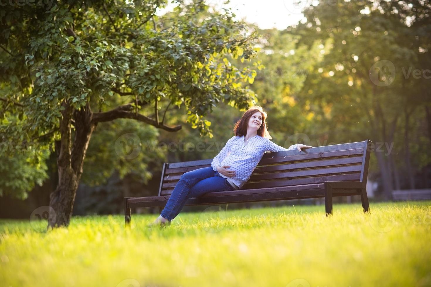 schöne junge schwangere Frau, die den Sonnenuntergang im Herbstpark genießt foto