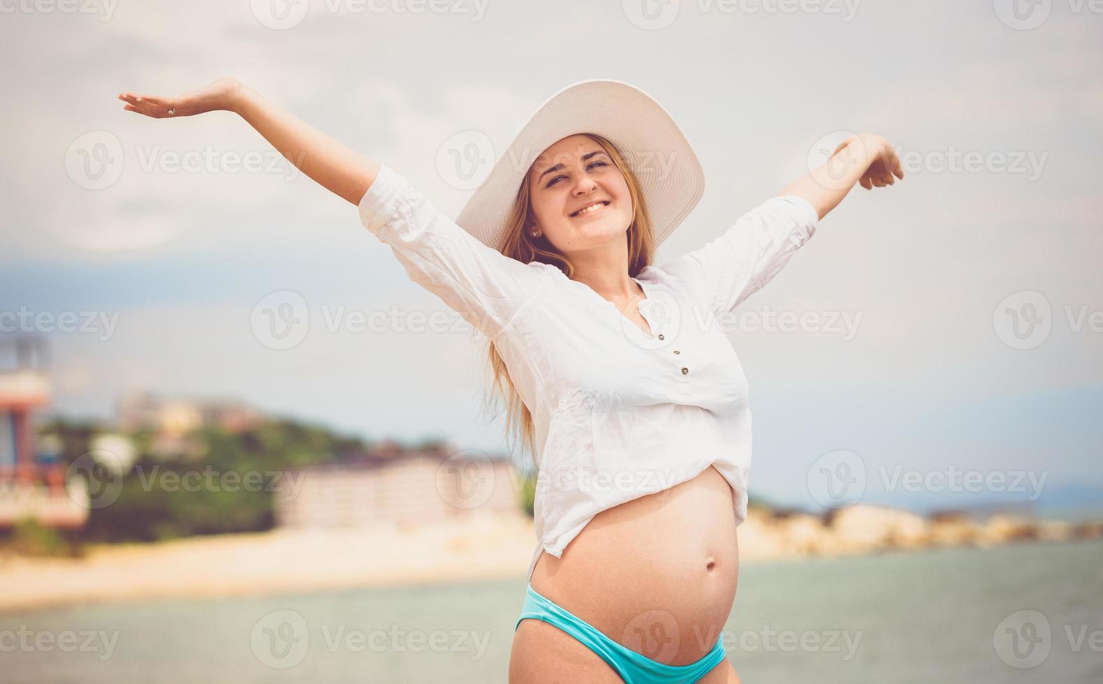 glückliche schwangere Frau im weißen Hemd, das Sonne am Strand genießt foto