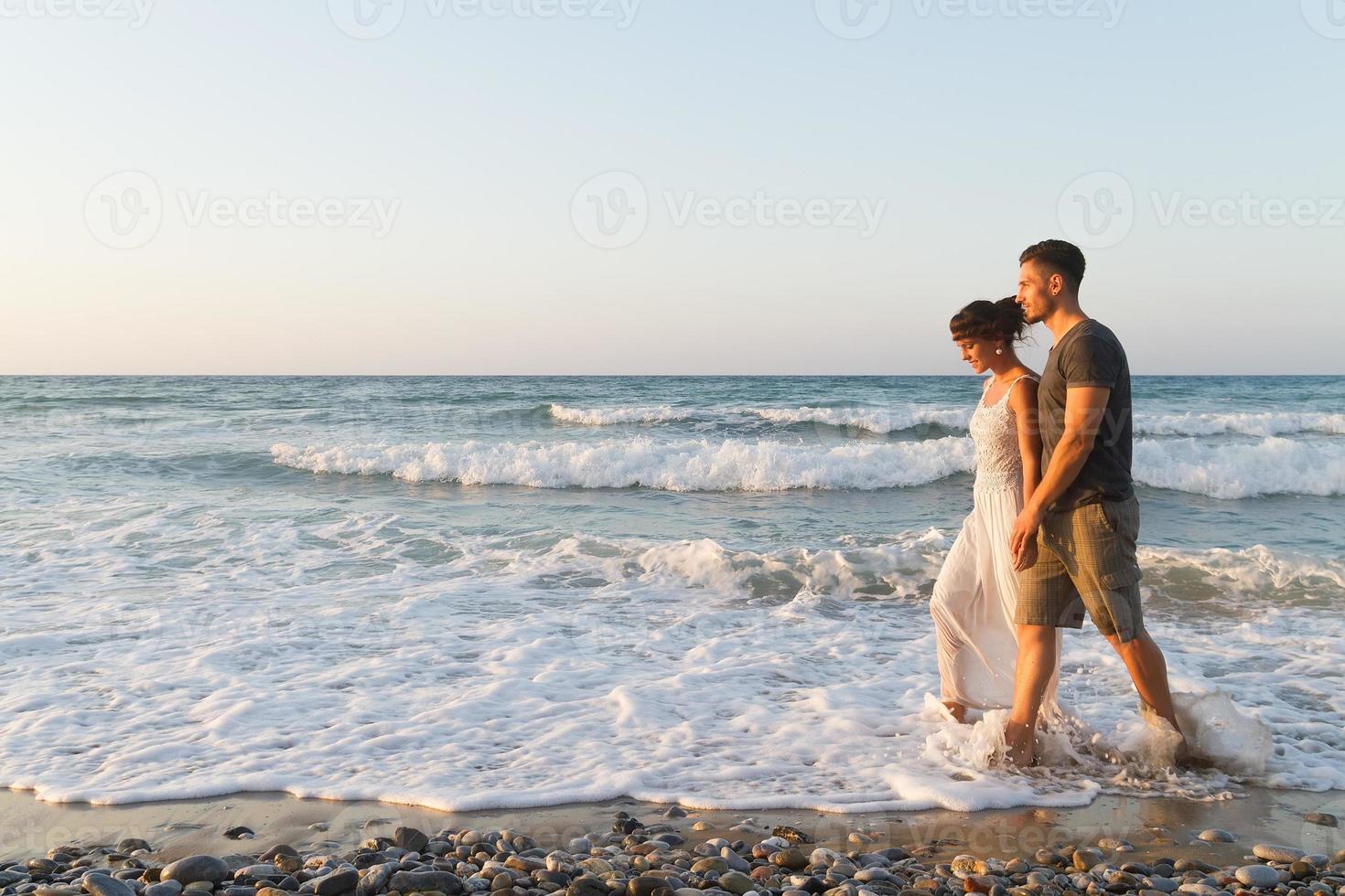 junges Paar geht gerne in der Abenddämmerung an einem dunstigen Strand spazieren foto
