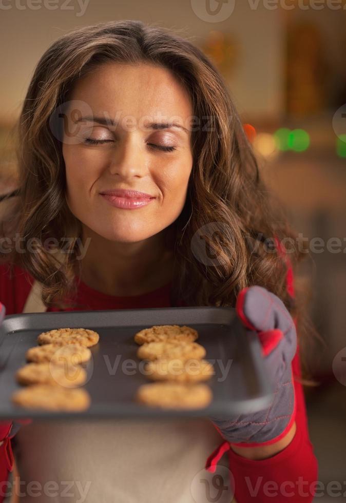 glückliche junge Hausfrau, die Geruch von Weihnachtsplätzchen auf Pfanne genießt foto