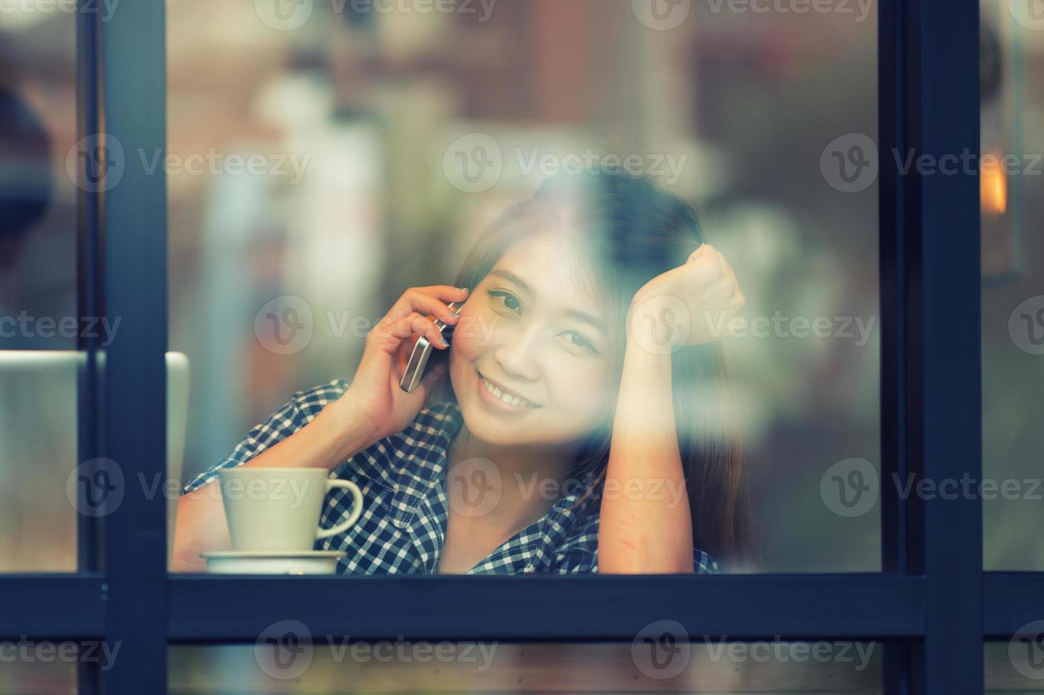 Asien lächeln Frau, die Telefon im Café spricht und Kaffee genießt foto