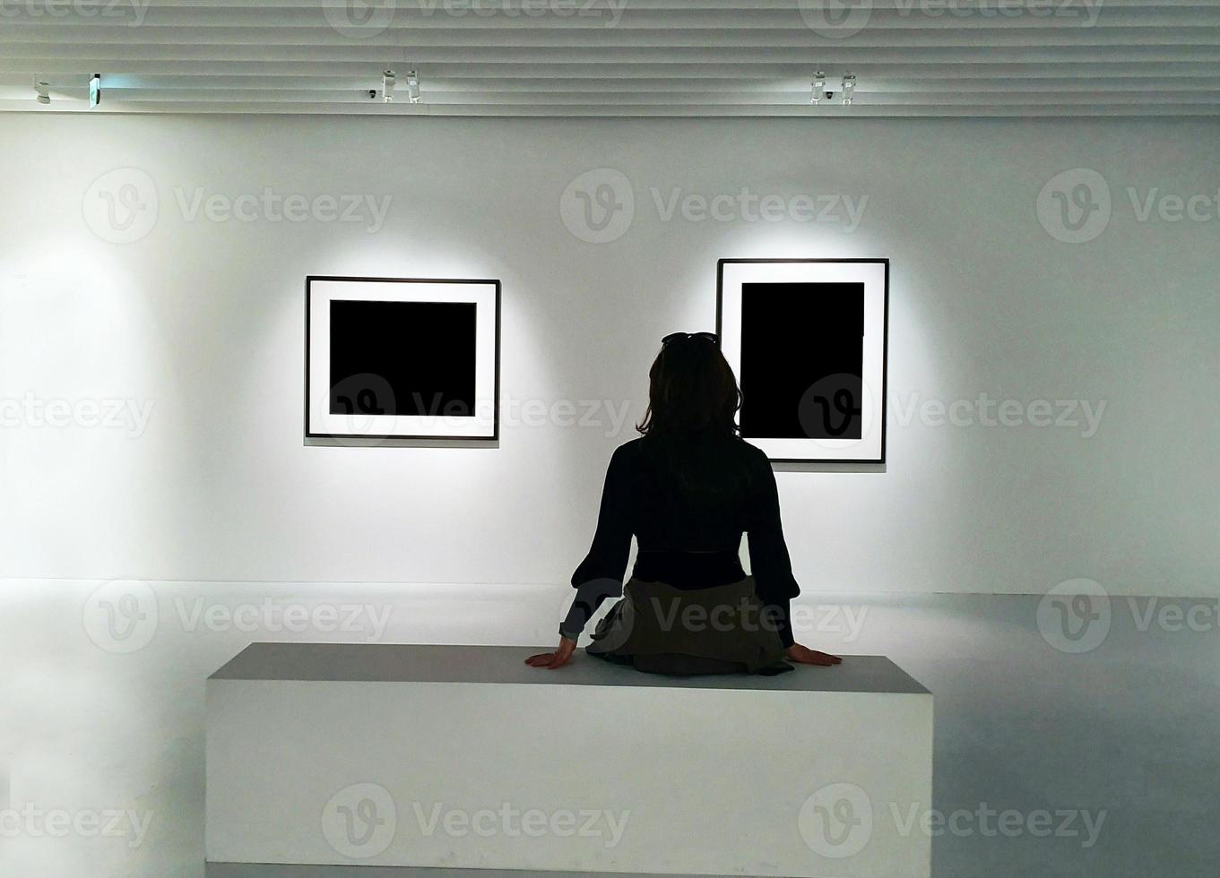 Rückseite der Frau im schwarzen Kleid, die auf der Bank im Kunstmuseum sitzt foto
