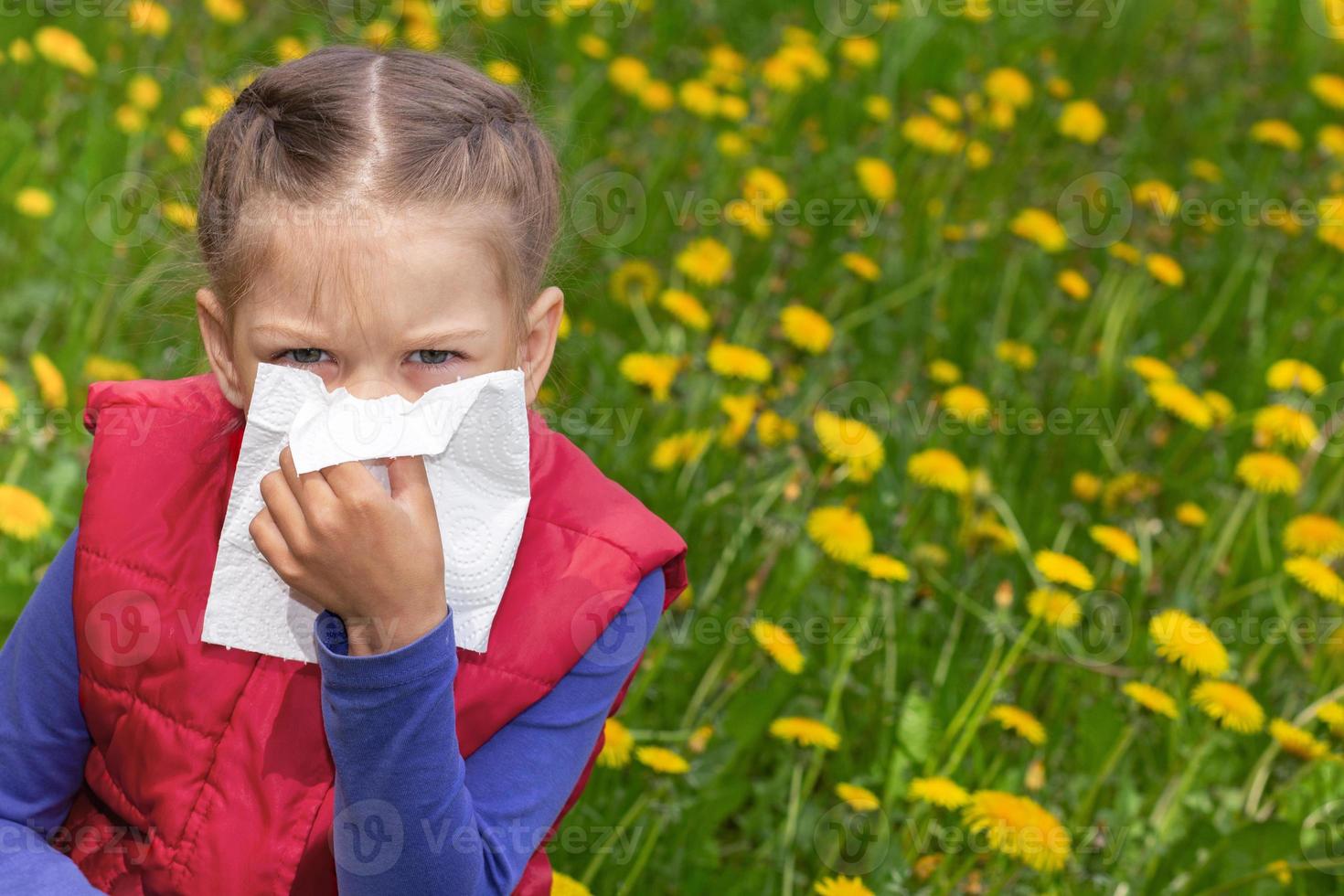 Kind mit Serviette, die Nase von Hand auf Löwenzahnrasen abwischt foto