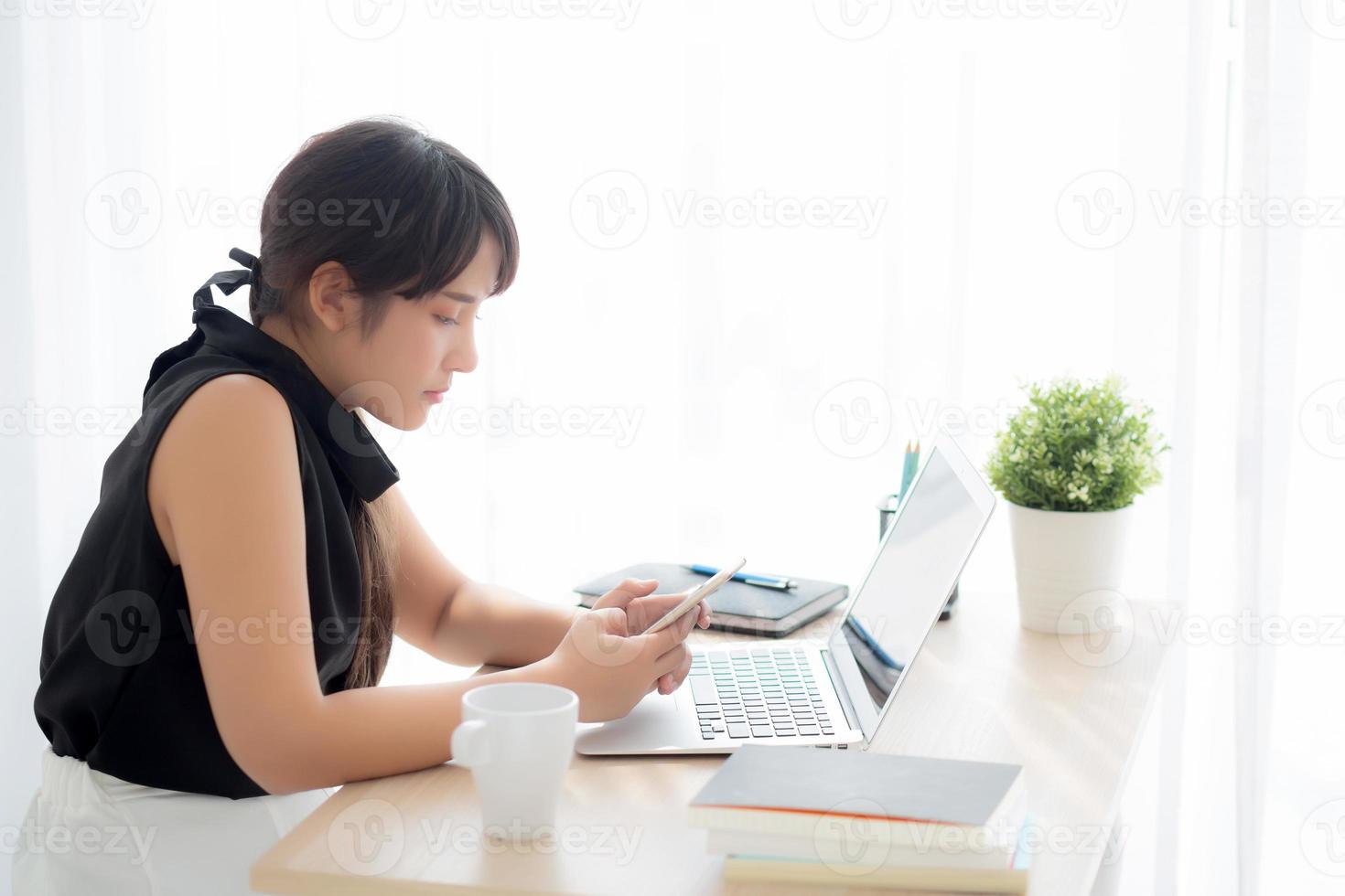 schöne junge asiatische frau, die laptop-computer online zum internet arbeitet und sms-nachricht auf intelligentem handy, freiberuflich unter verwendung des notizbuch-, geschäfts- und kommunikationskonzepts. foto