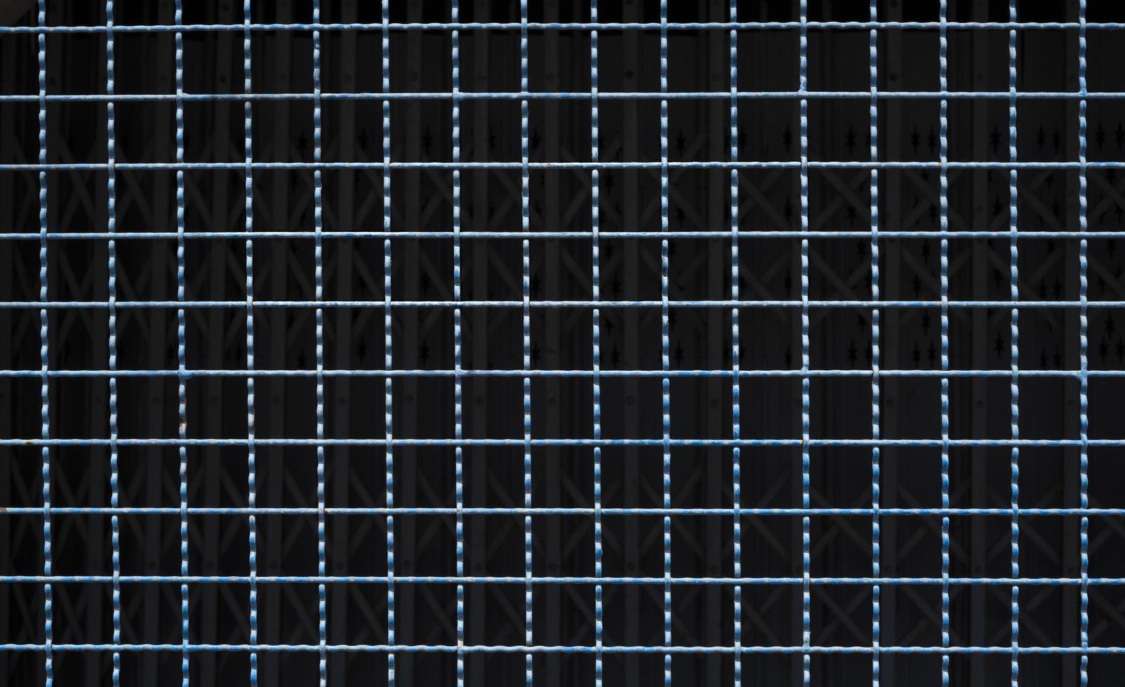 Nahaufnahme des Gittermusters des alten blauen Stahlgitterzauns mit verschwommener Verschlusstür im dunklen Hintergrund foto