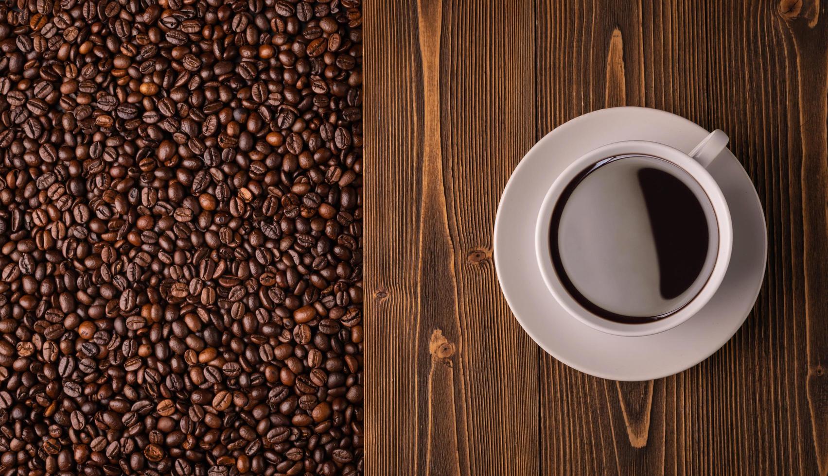 geröstete kaffeebohnen und kaffeetasse auf holzstruktur. braune kaffeebohnenbeschaffenheit der draufsicht für hintergrund- und tapetengebrauch foto