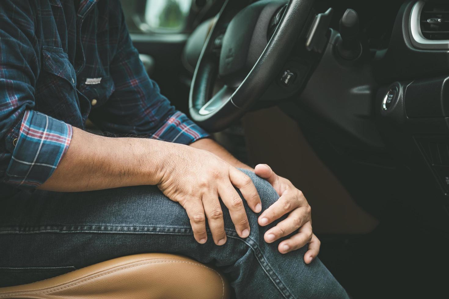 Der Mensch hält und massiert sein Knie im Auto mit den Händen, während er anhält. Außenaufnahmen für Transport und Gesundheitswesen foto