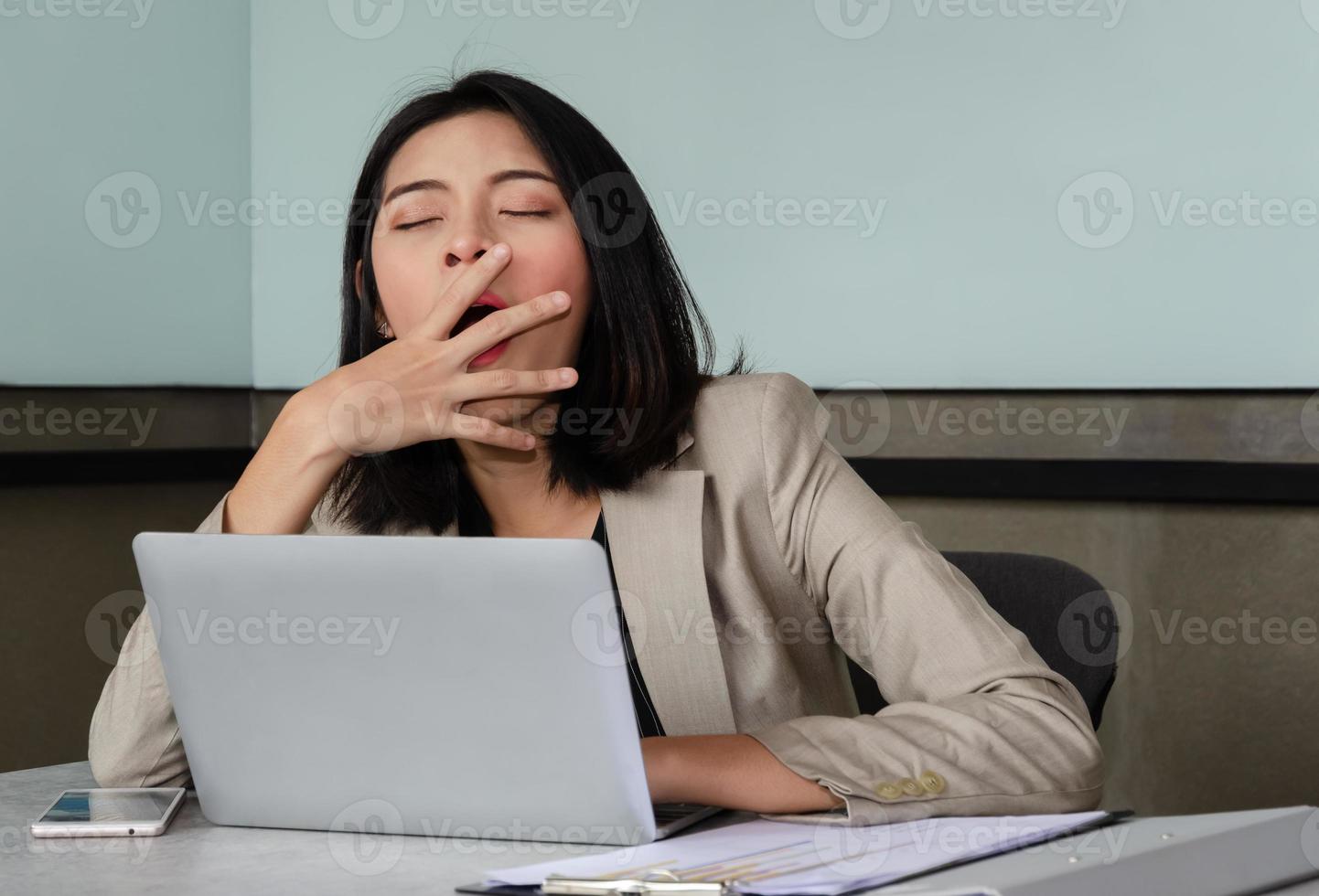 Junge Geschäftsfrau gähnt am Besprechungstisch vor dem Laptop und bedeckt ihren Mund aus Höflichkeit. überarbeitungs- und schlafentzugskonzept foto