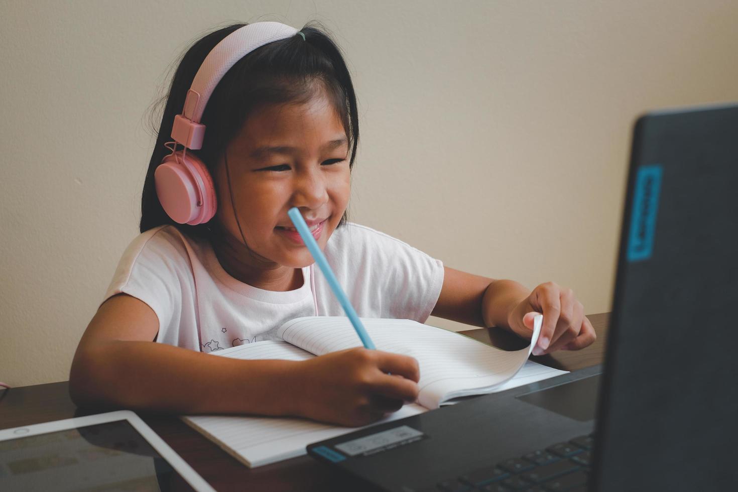 thailändisches mädchen im online-lernkurs zu hause während der covid-19-situation. schüler, der während der quarantäne das buch und das lernformular schreibt. ausgewählten Fokus. online-bildung, hausschulkonzept. foto