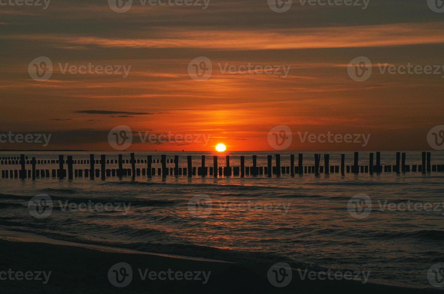 sonnenuntergang in zingst am meer. rot-orangefarbene Sonne geht am Horizont unter. Möwen kreisen am Himmel foto