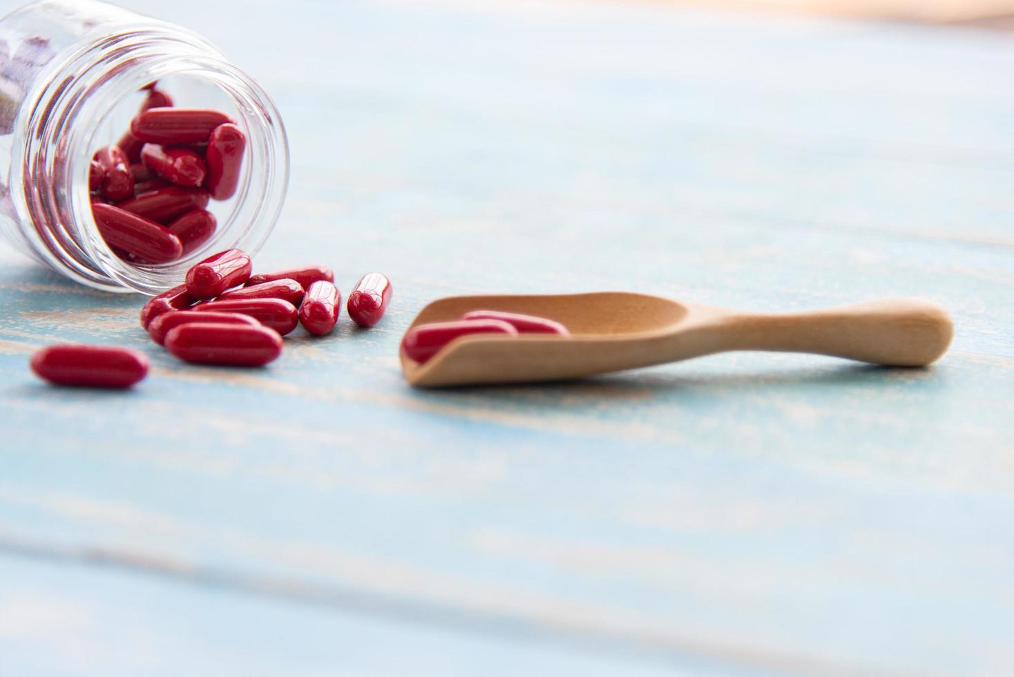 rote medikamente in den glasflaschen auf dem holzlöffel und dem blauen tisch. pharmazeutische Medizin oder Vitaminpillen, Tabletten und Kapseln foto